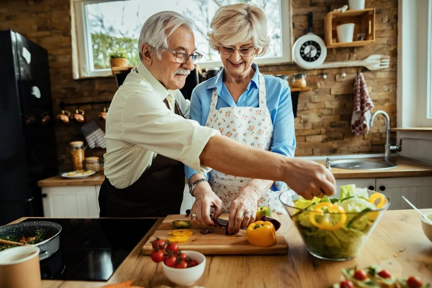 Glückliches älteres Paar macht Salat, während es gemeinsam in der Küche Essen zubereitet.